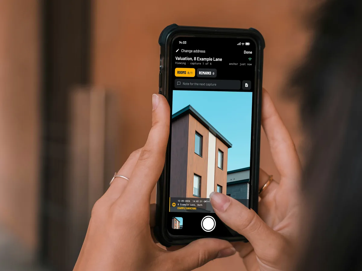 Two hands hold a phone with the EverStamp camera, with the front of a house in the viewfinder
