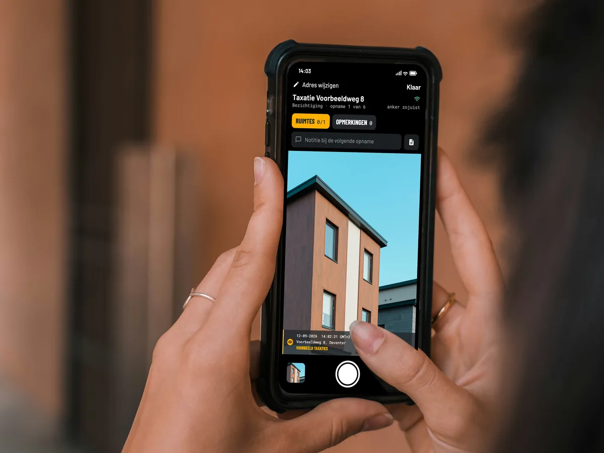 Twee handen houden een telefoon met de camera van EverStamp, met de gevel van een woning in de zoeker