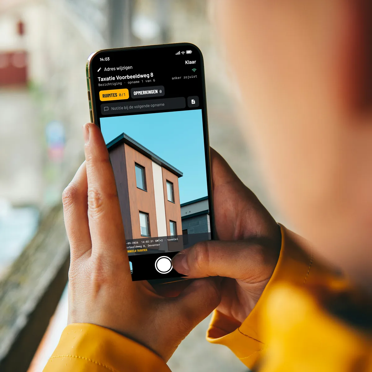Over de schouder gezien: twee handen houden een telefoon met de camera van EverStamp open bij een taxatie